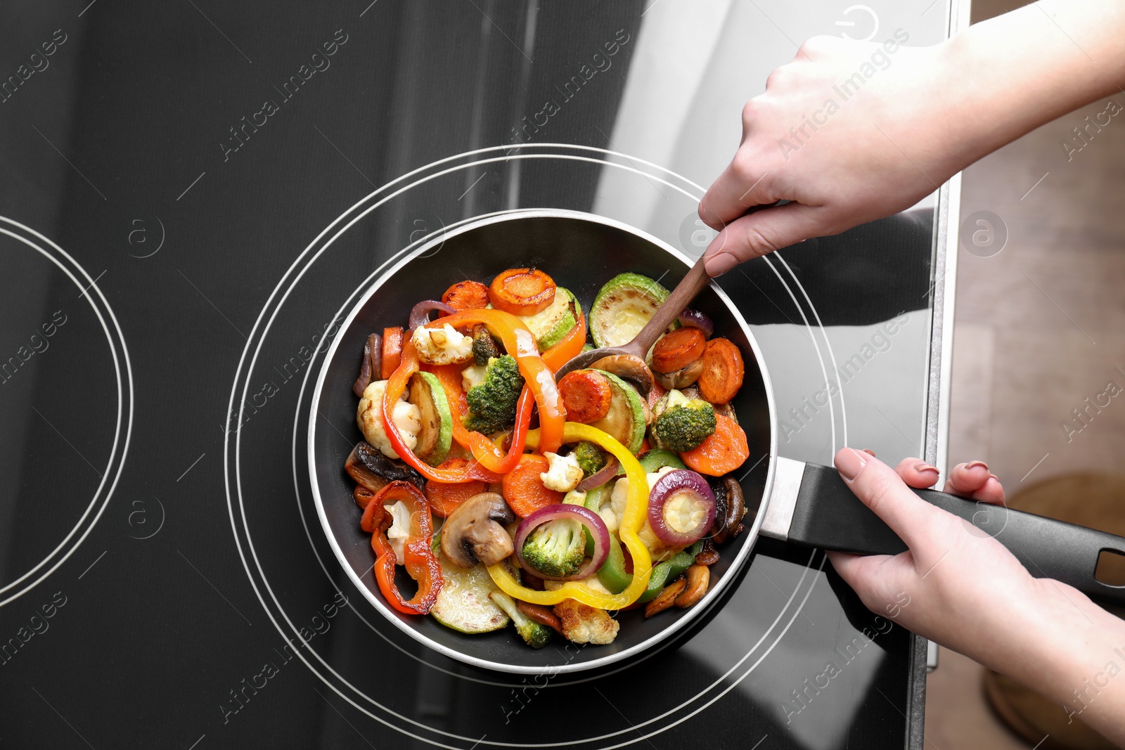 Photo of Woman cooking vegetables and mushrooms in frying pan on cooktop indoors, top view