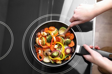 Photo of Woman cooking vegetables and mushrooms in frying pan on cooktop indoors, top view