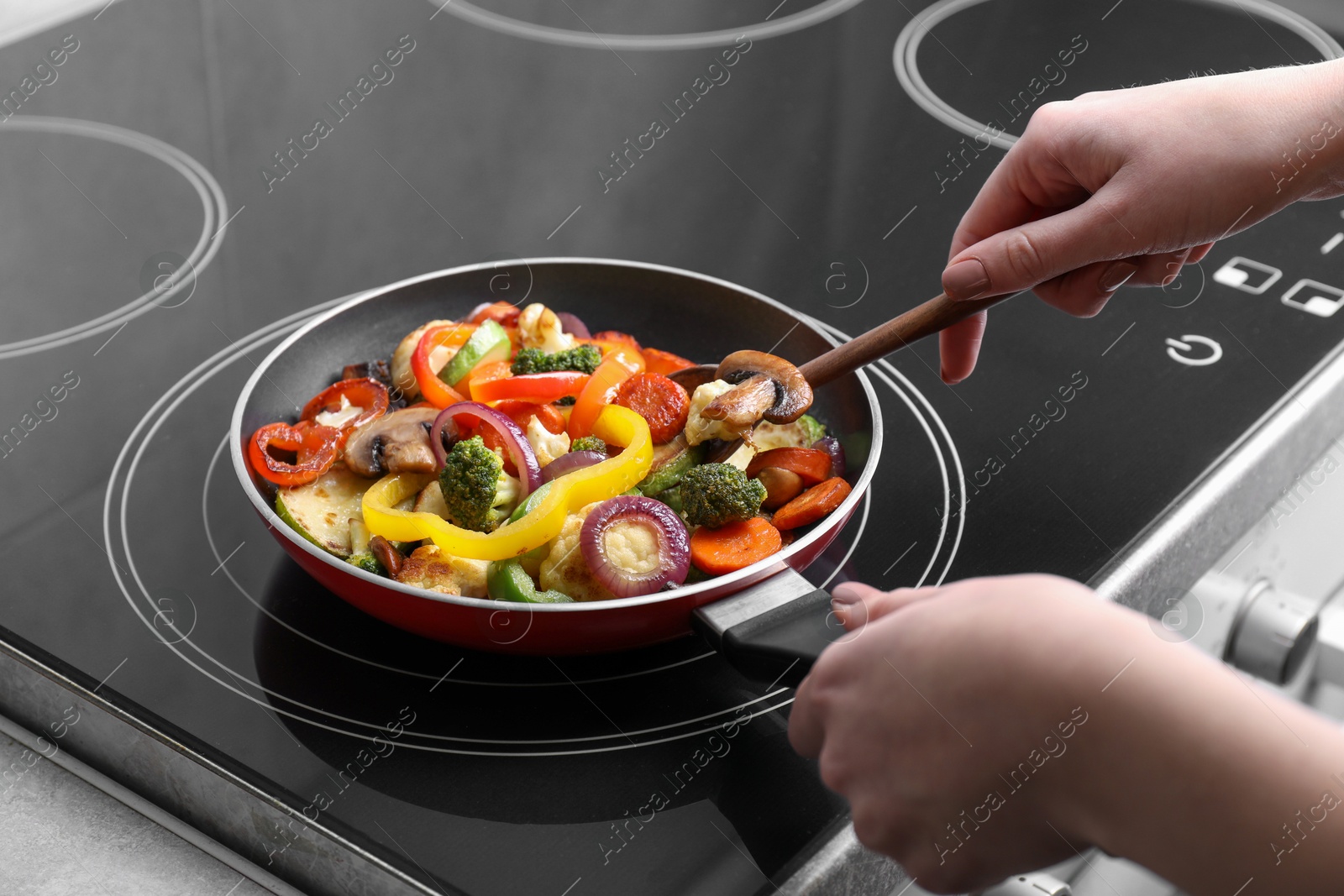 Photo of Woman cooking vegetables and mushrooms in frying pan on cooktop indoors, closeup