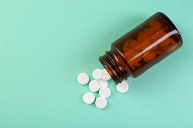 Photo of Bottle of antibiotic pills on turquoise background, top view. Space for text