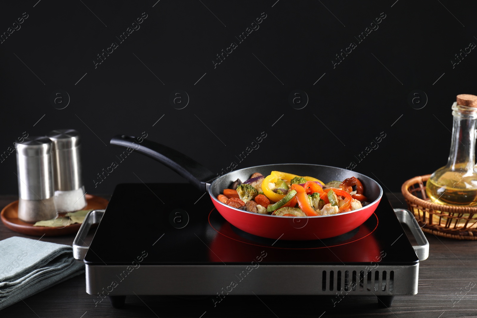 Photo of Frying pan with vegetables and stove on wooden table against black background