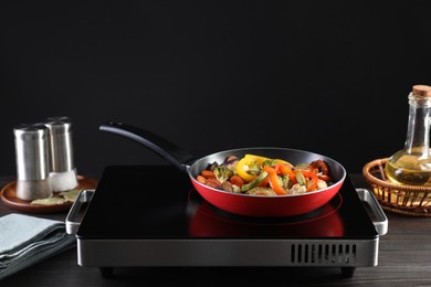 Photo of Frying pan with vegetables and stove on wooden table against black background