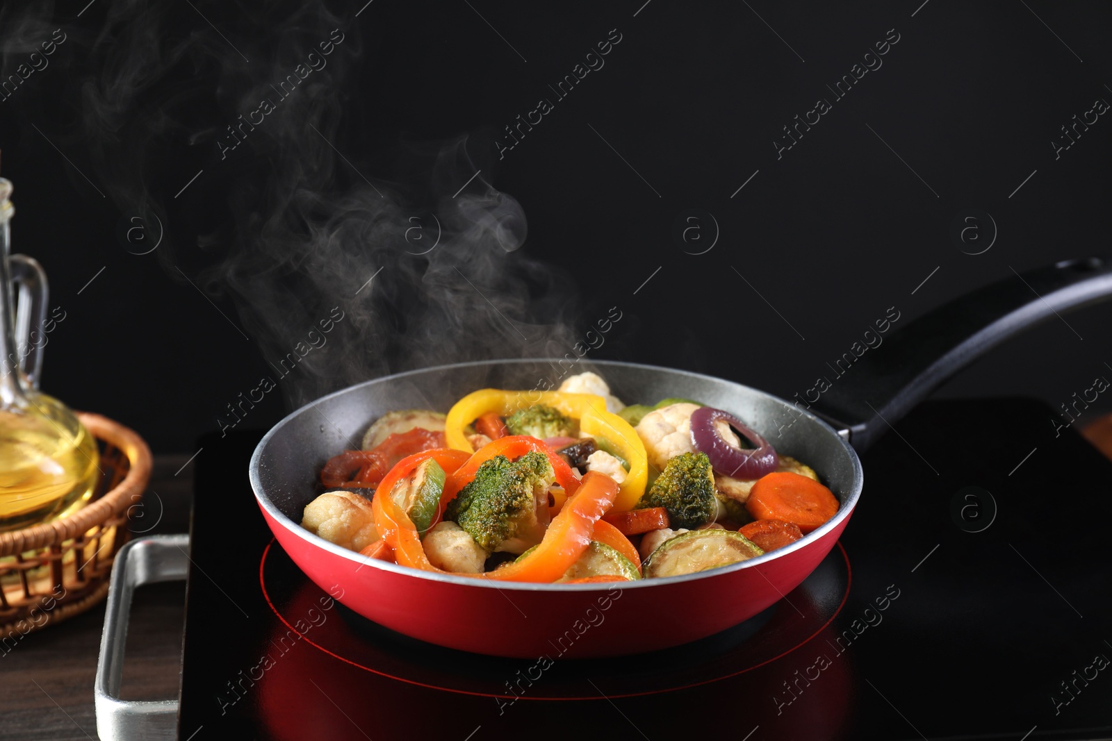 Photo of Frying pan with vegetables and stove on table against black background