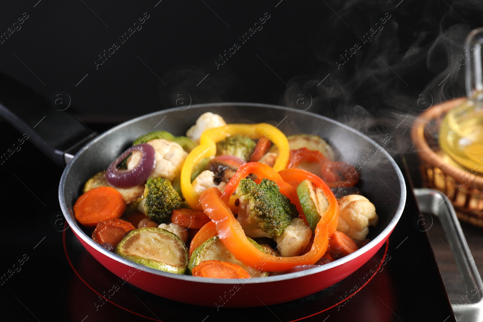 Photo of Frying pan with vegetables and stove on table against black background, closeup