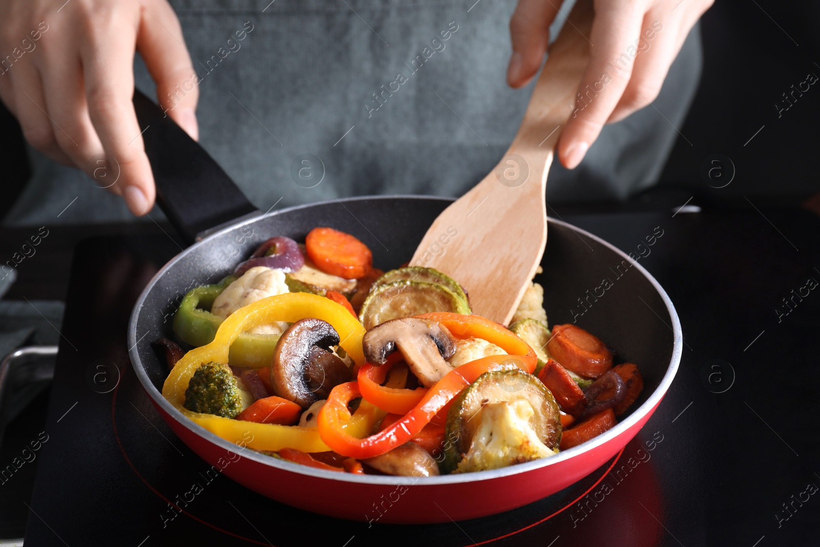 Photo of Woman frying vegetables and mushrooms in pan on stove, closeup