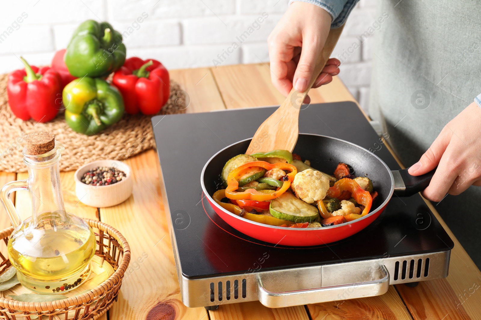 Photo of Woman frying vegetables in pan on stove at wooden table indoors, closeup