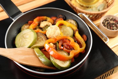 Photo of Frying pan with vegetables and stove on table, closeup