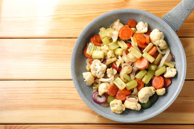 Photo of Frying pan with vegetables on wooden table, top view. Space for text