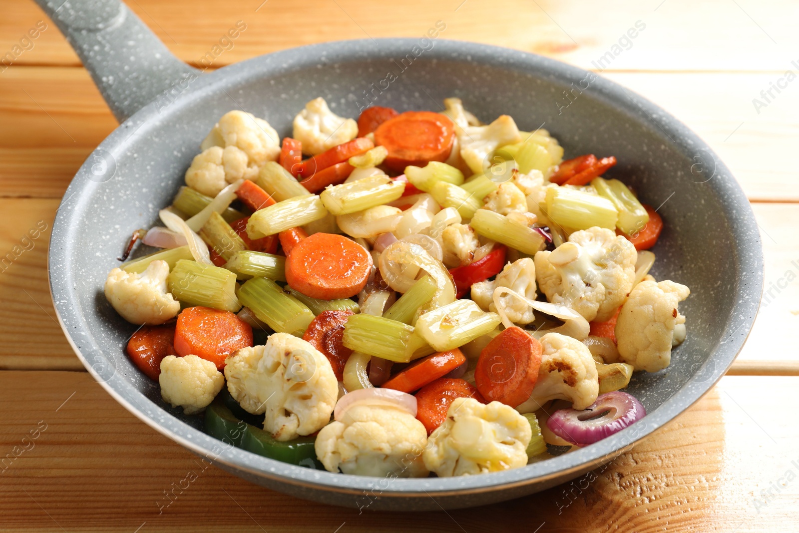 Photo of Frying pan with vegetables on wooden table, closeup