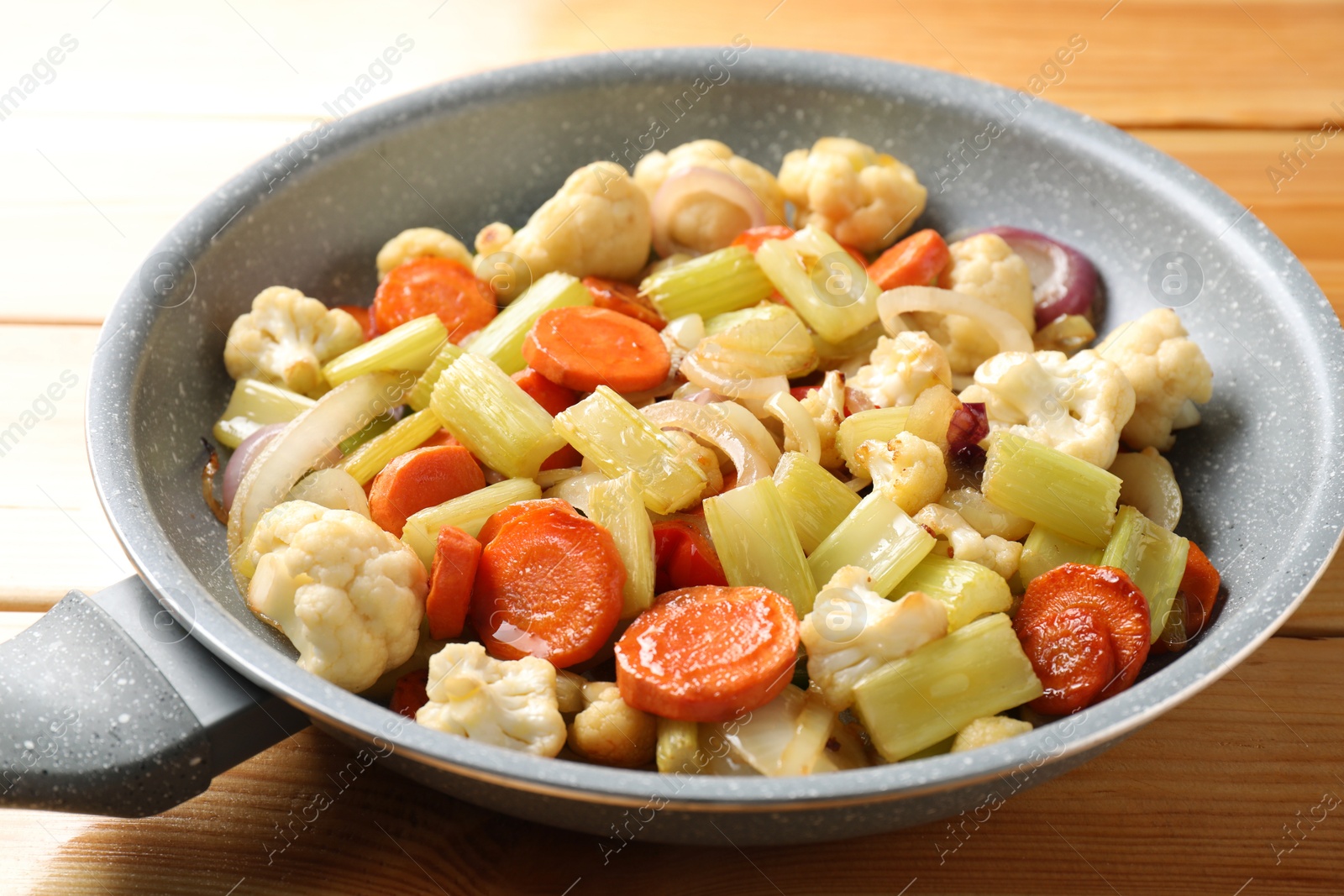 Photo of Frying pan with vegetables on wooden table, closeup