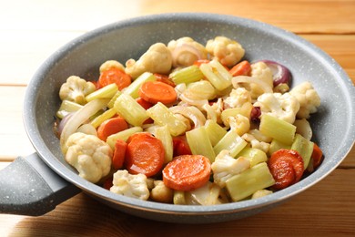 Photo of Frying pan with vegetables on wooden table, closeup