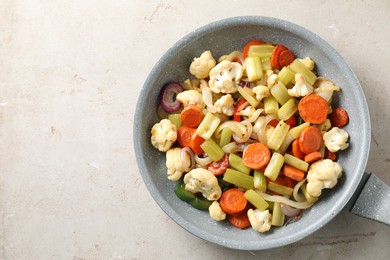 Photo of Frying pan with vegetables on light textured table, top view. Space for text