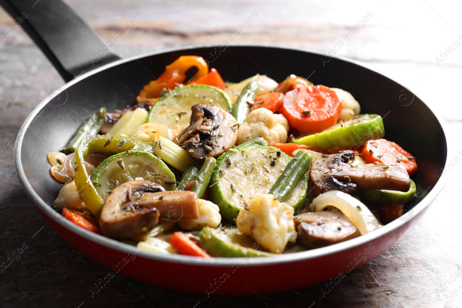 Photo of Different vegetables and mushrooms in frying pan on grey textured table, closeup