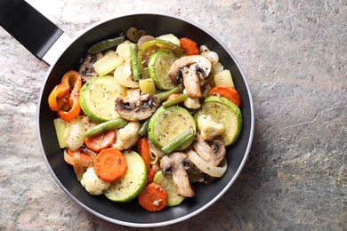 Photo of Different vegetables and mushrooms in frying pan on grey textured table, top view