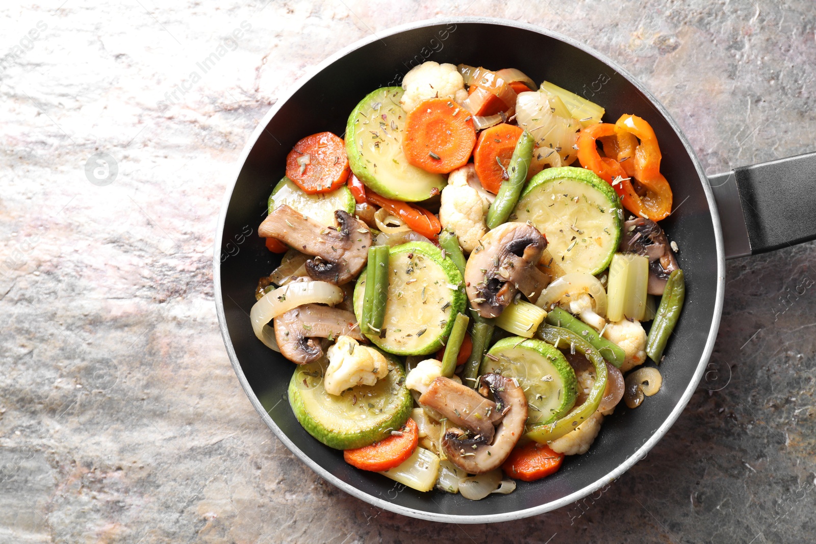 Photo of Different vegetables and mushrooms in frying pan on grey textured table, top view