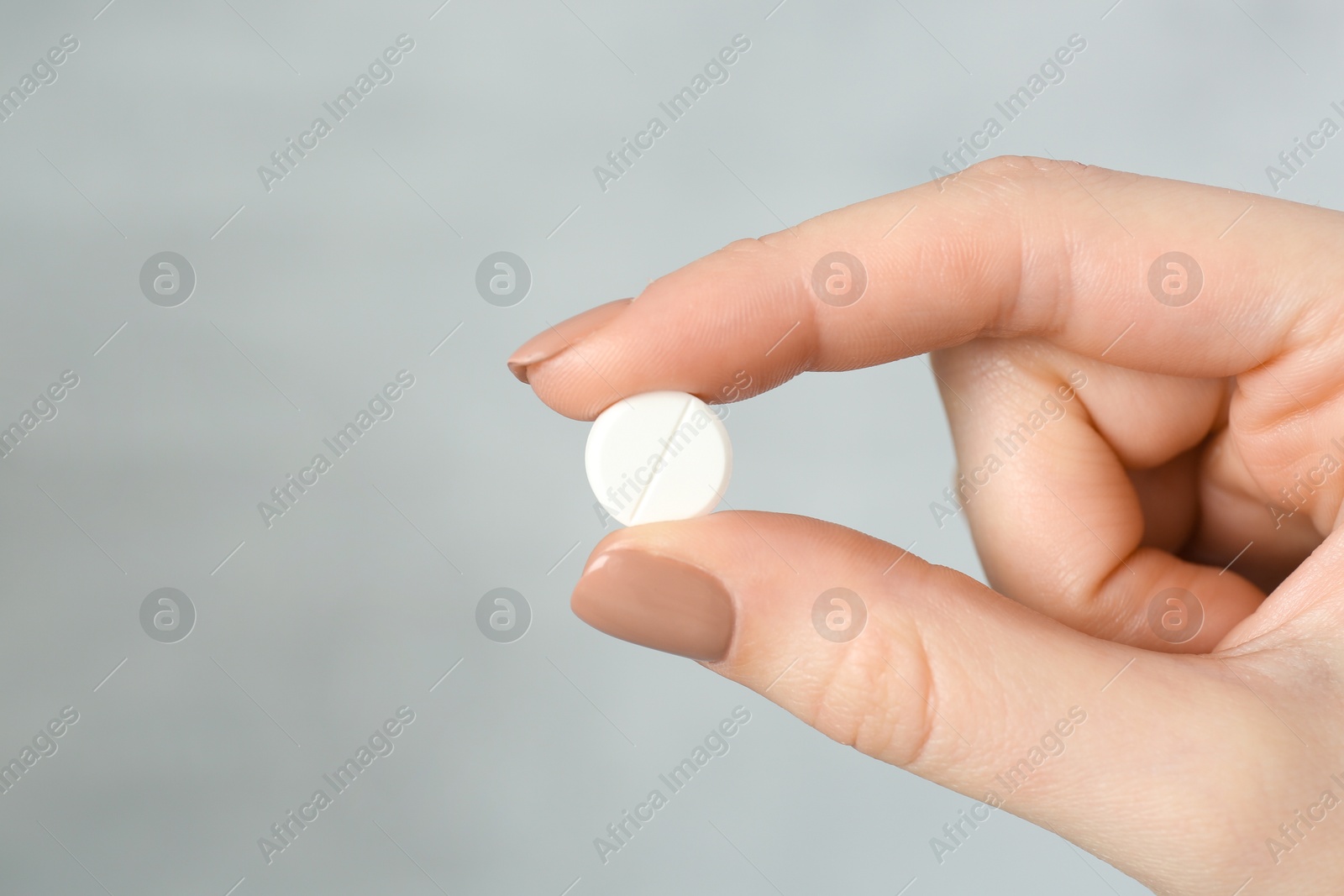 Photo of Woman holding antibiotic pill against grey background, closeup. Space for text