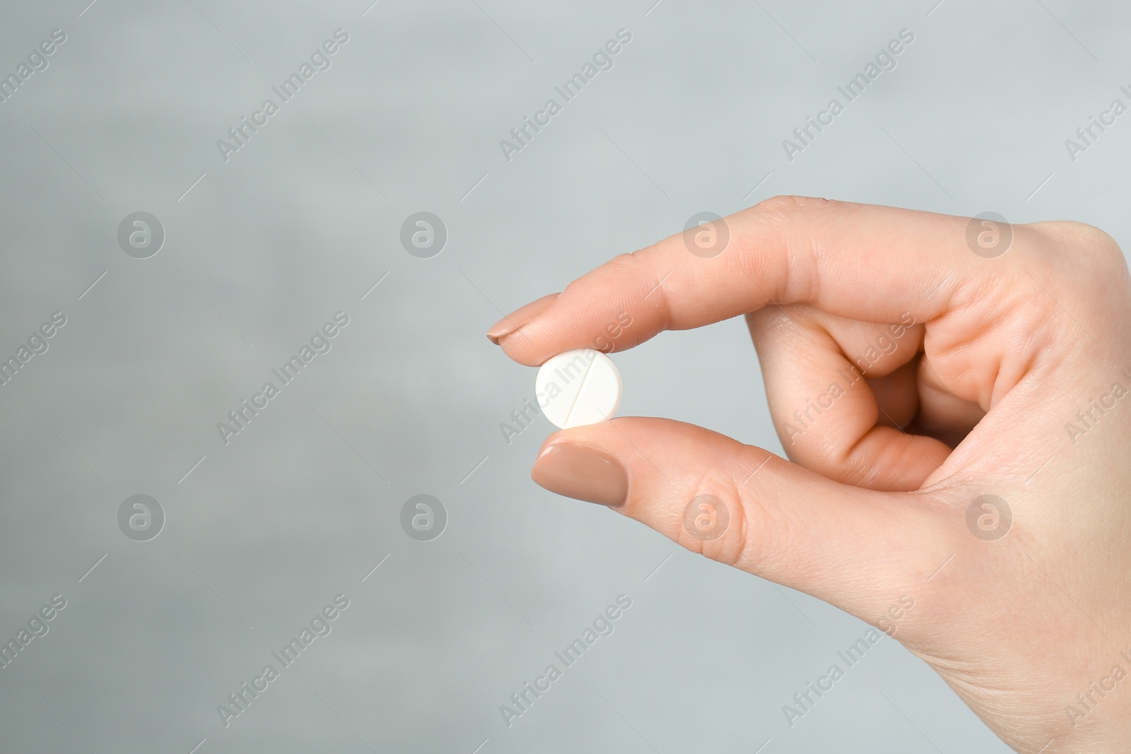 Photo of Woman holding antibiotic pill against grey background, closeup. Space for text