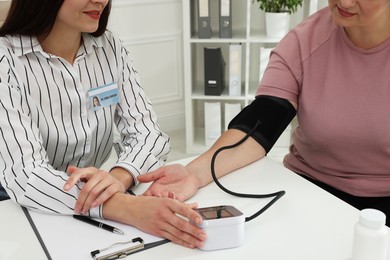 Photo of Nutritionist measuring overweight woman's blood pressure at desk in hospital, closeup