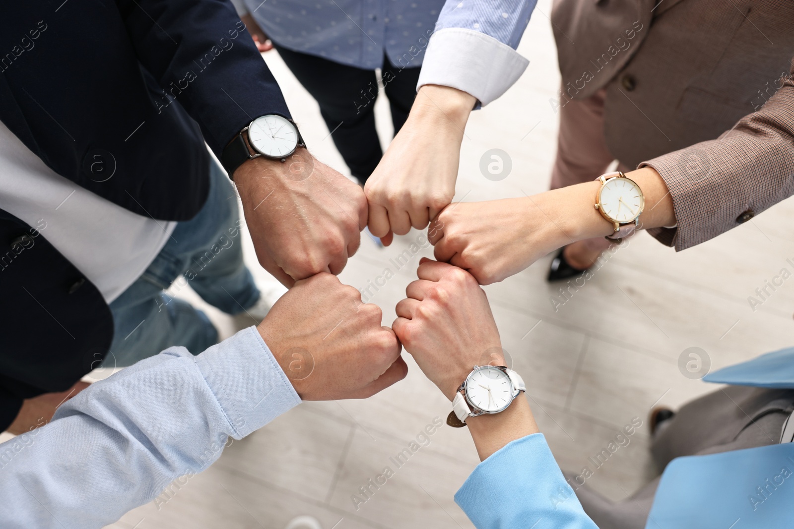 Photo of Teamwork. Group of people joining fists together indoors, top view