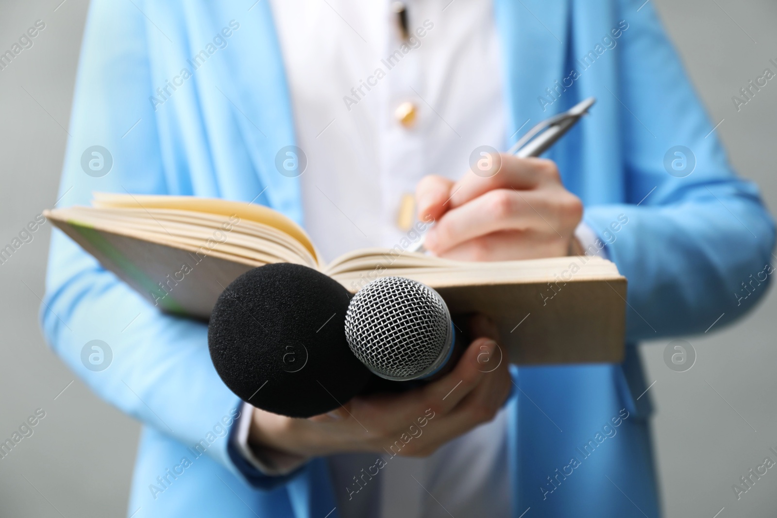 Photo of Journalist with microphones taking notes on grey background, closeup