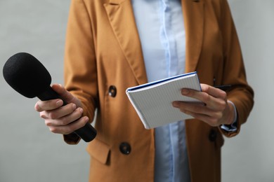 Photo of Journalist with microphone and notebook on grey background, closeup