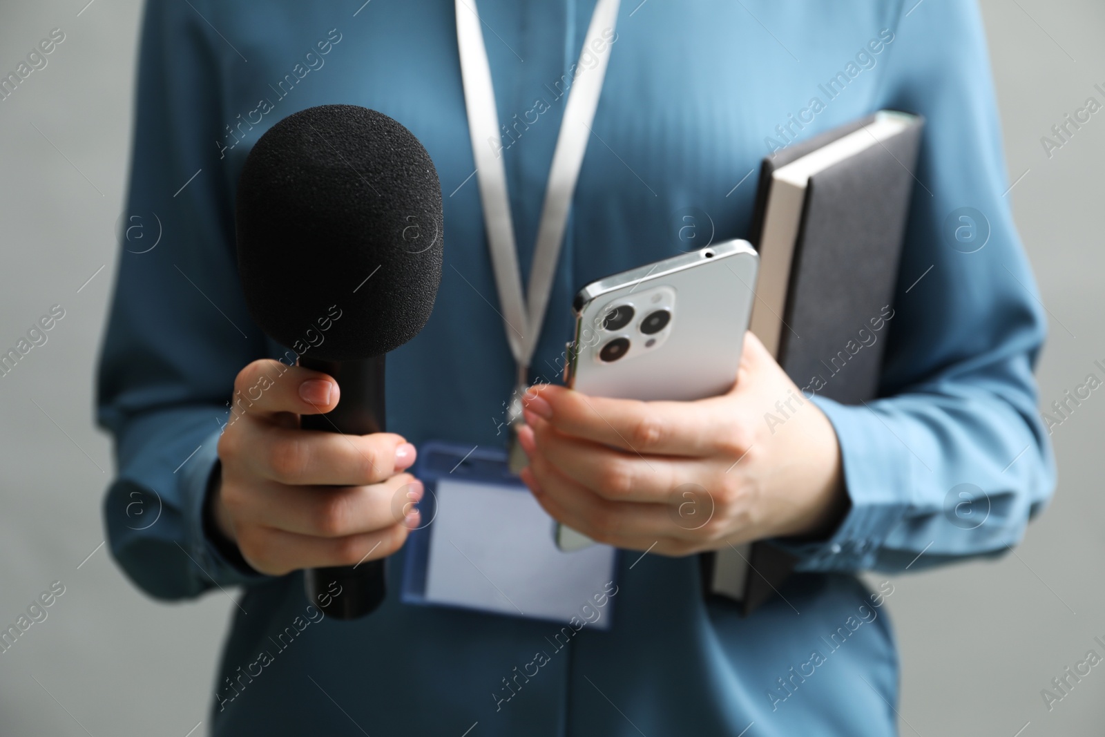 Photo of Journalist with microphone, smartphone and notebook on grey background, closeup