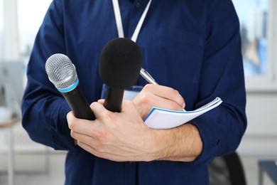 Photo of Journalist with microphones taking notes indoors, closeup