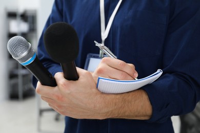 Photo of Journalist with microphones taking notes indoors, closeup