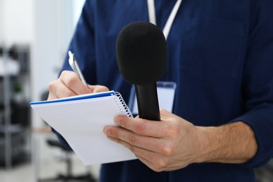 Photo of Journalist with microphone taking notes indoors, closeup