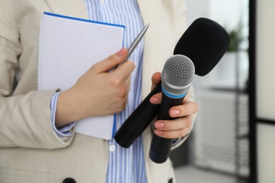 Photo of Journalist with microphones, notebook and pen indoors, closeup