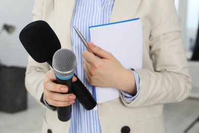 Photo of Journalist with microphones, notebook and pen indoors, closeup