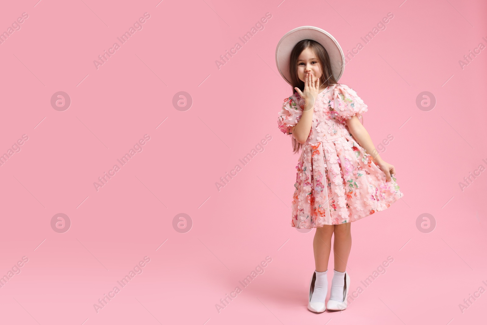 Photo of Stylish little girl wearing oversized high heeled shoes on pink background, space for text