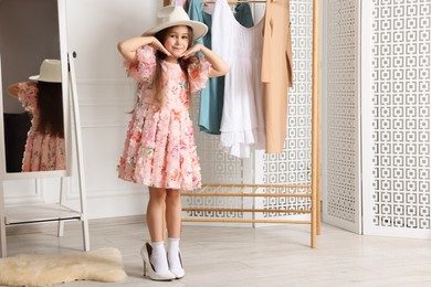 Photo of Stylish little girl wearing oversized high heeled shoes indoors