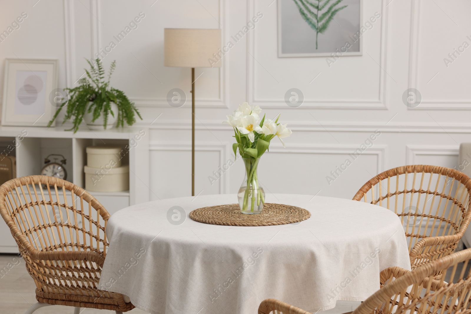 Photo of Table with white tablecloth, flowers in vase and chairs in stylish room. Interior design