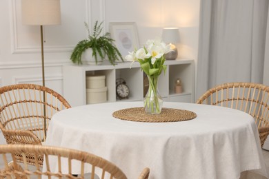 Photo of Table with white tablecloth, flowers in vase and chairs in stylish room. Interior design