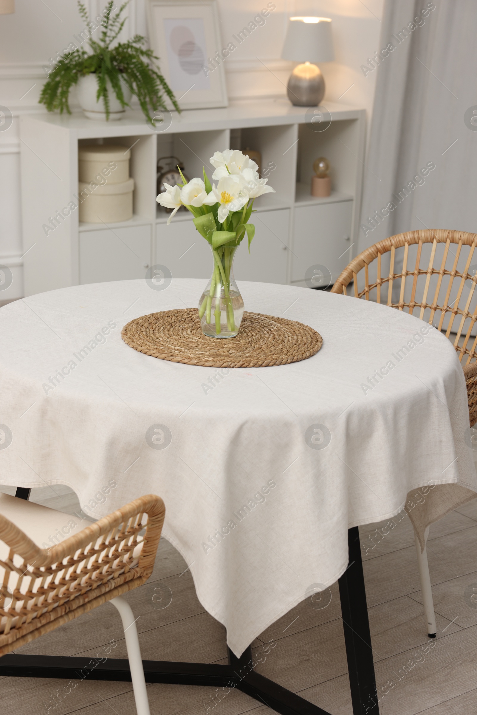 Photo of Table with white tablecloth, flowers in vase and chairs in stylish room. Interior design