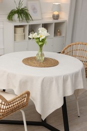 Table with white tablecloth, flowers in vase and chairs in stylish room. Interior design