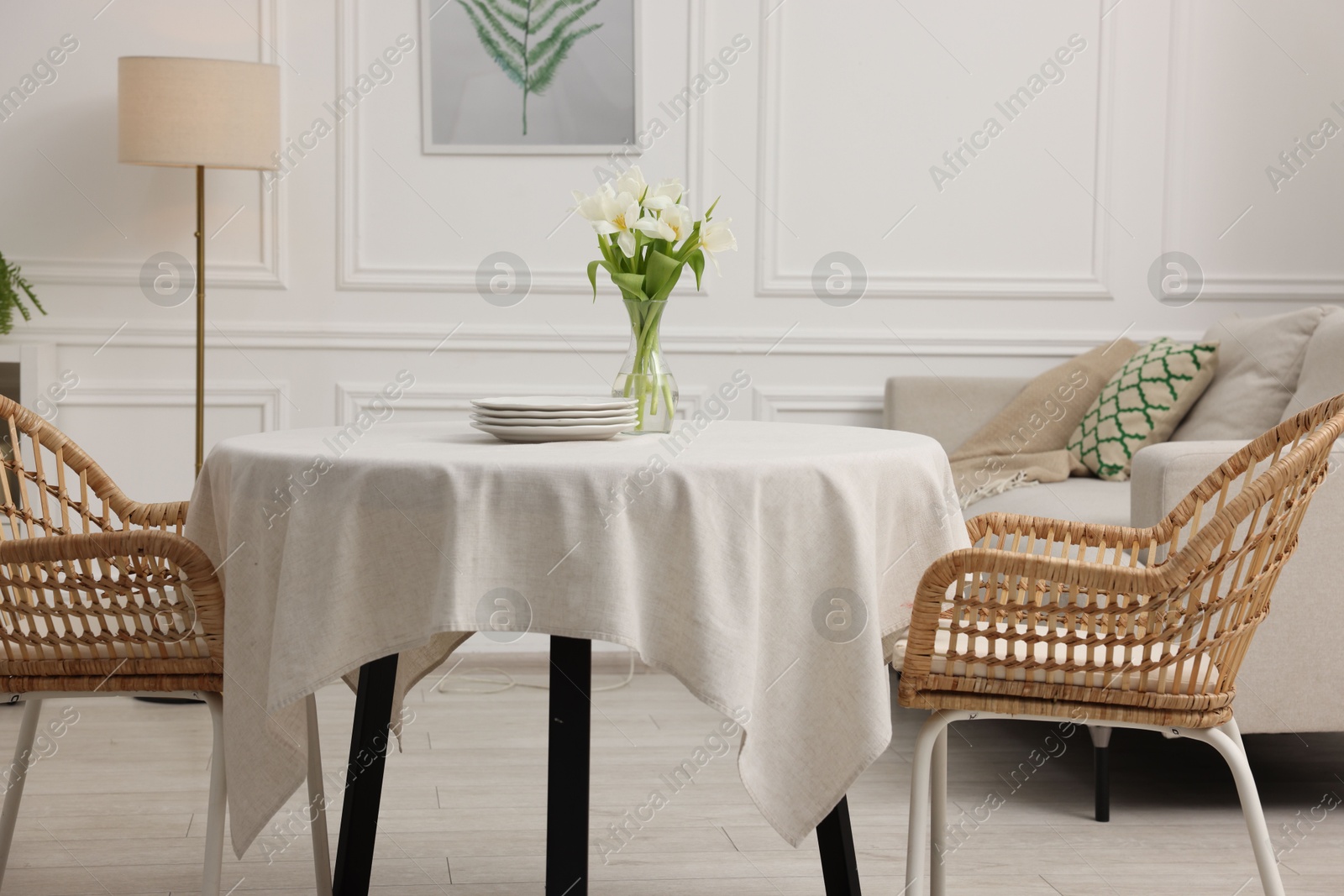 Photo of Table with white tablecloth, flowers in vase and chairs in stylish room. Interior design