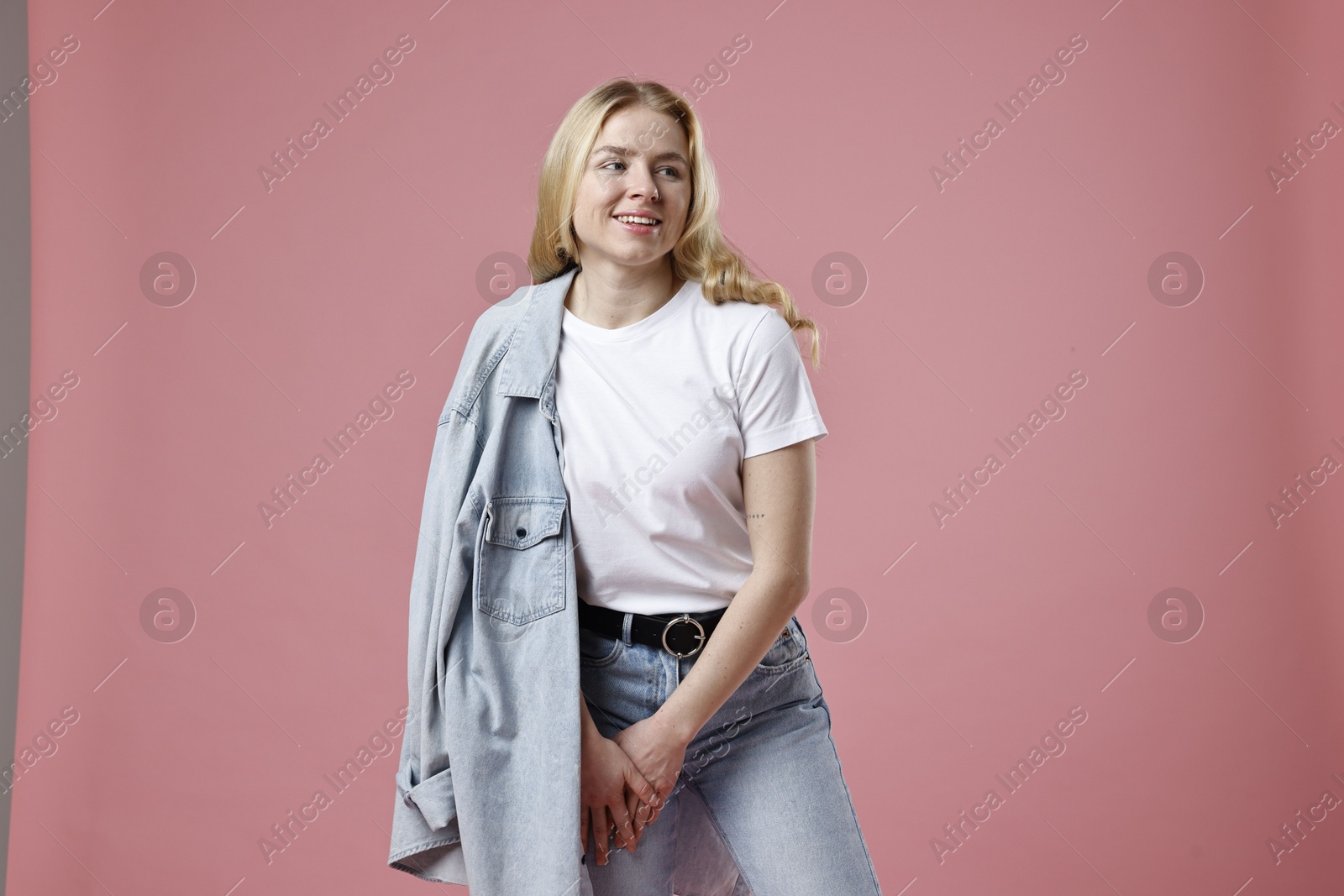 Photo of Smiling woman in stylish jeans on pink background