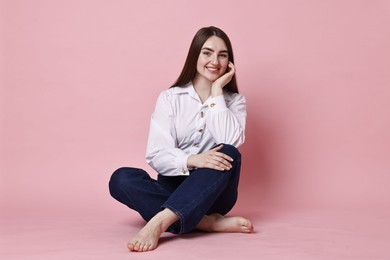 Photo of Smiling woman in stylish jeans on pink background