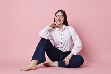 Photo of Smiling woman in stylish jeans on pink background