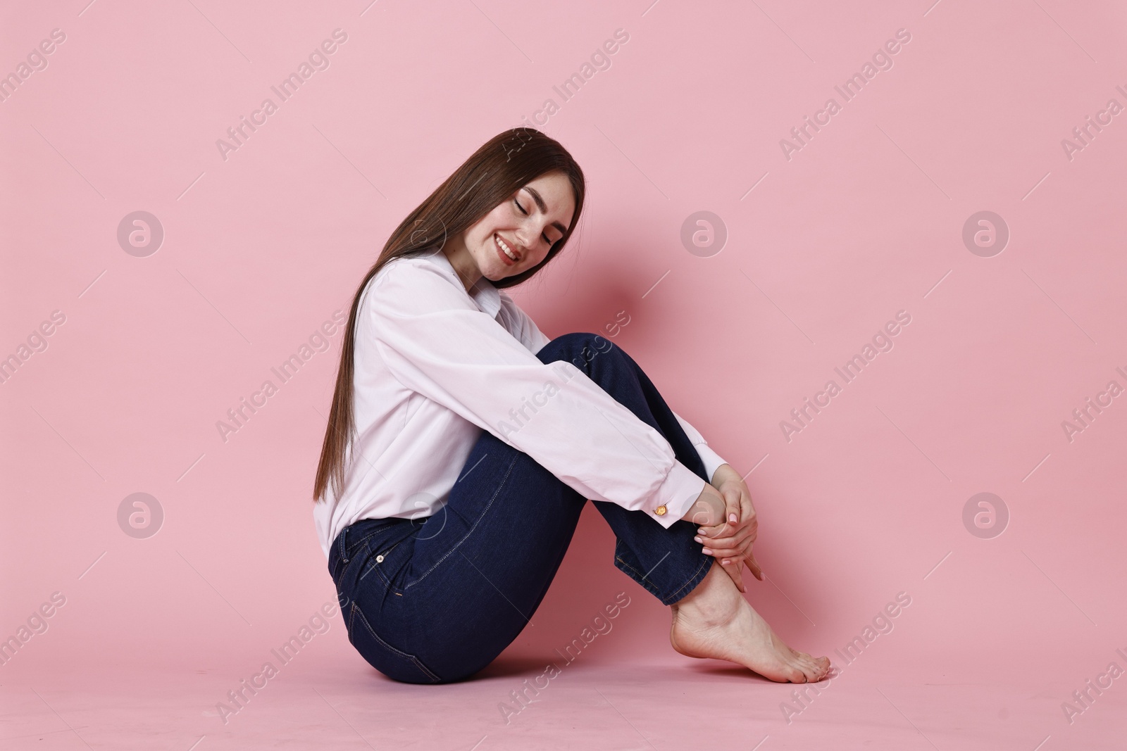 Photo of Smiling woman in stylish jeans on pink background