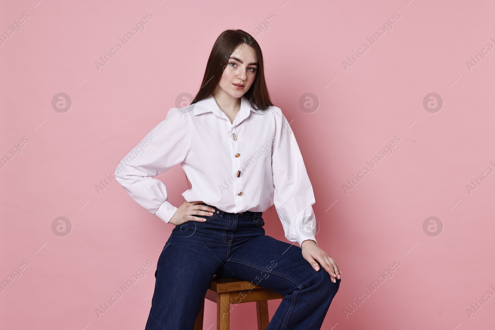 Photo of Beautiful young woman in stylish jeans sitting on stool against pink background