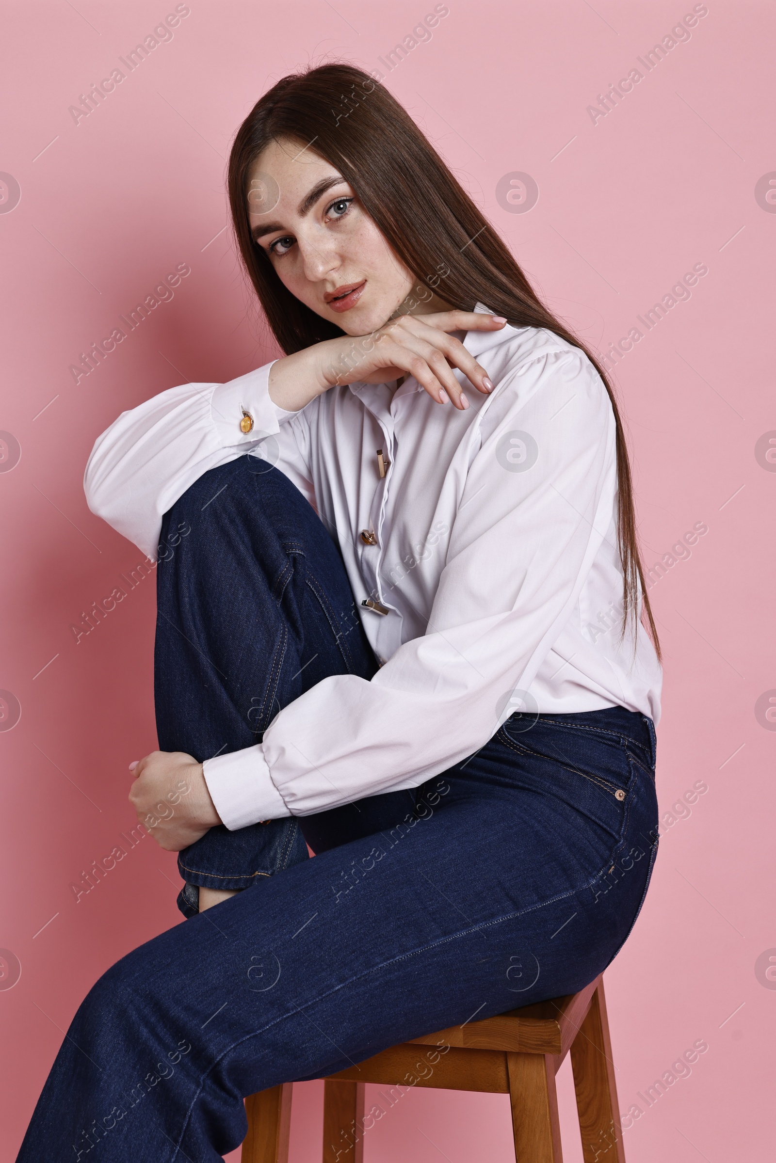 Photo of Beautiful young woman in stylish jeans sitting on stool against pink background