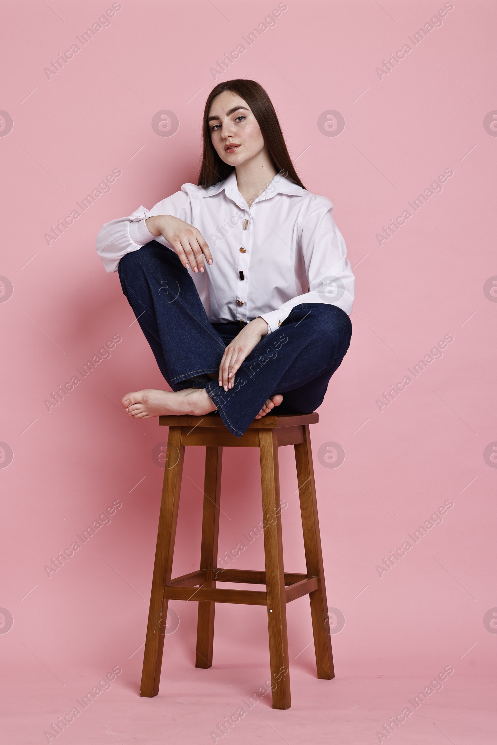 Photo of Beautiful young woman in stylish jeans sitting on stool against pink background