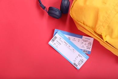 Photo of Airplane tickets, headphones and backpack on red background, flat lay with space for text. Travel abroad