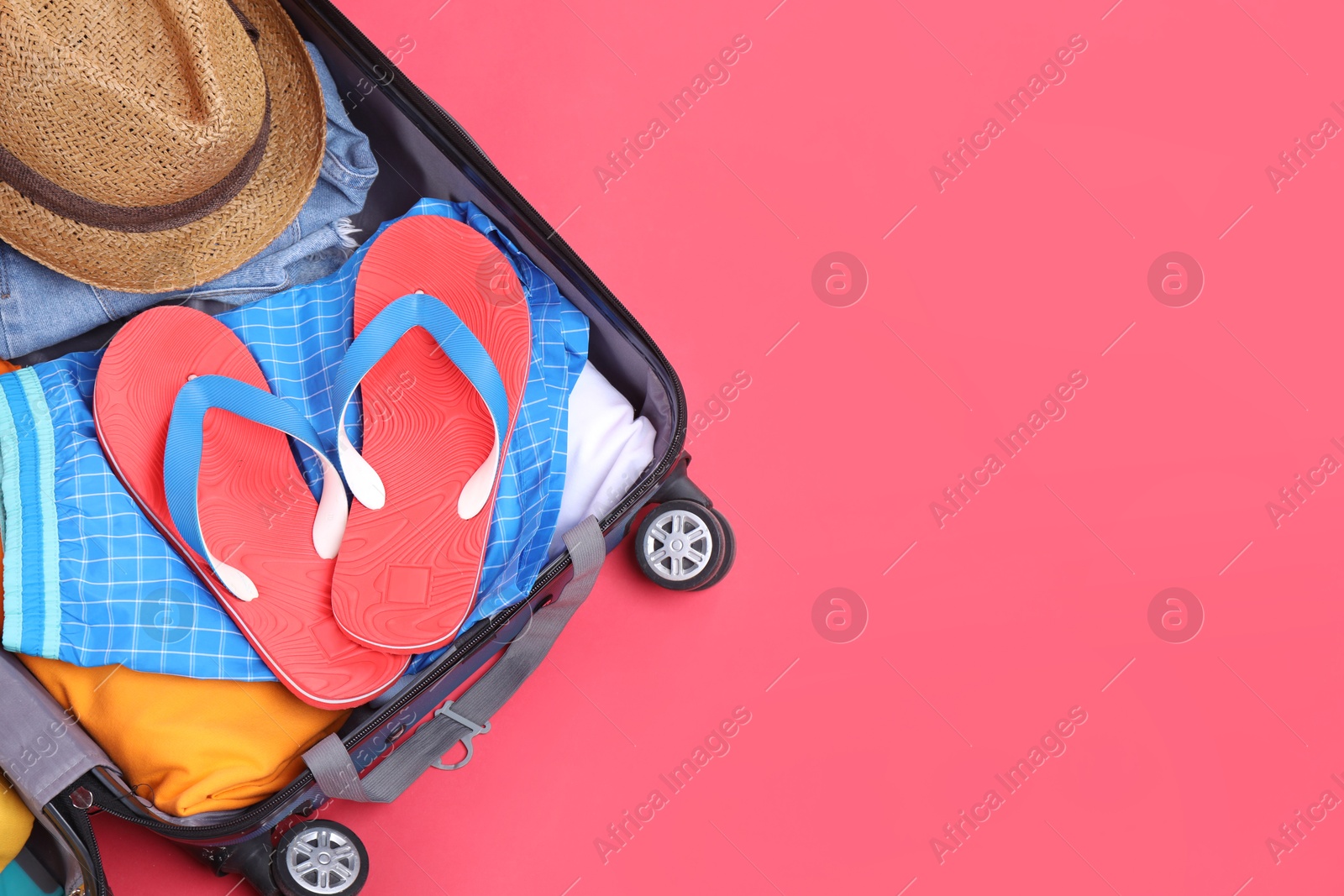 Photo of Travel abroad. Packed suitcase on red background, top view. Space for text