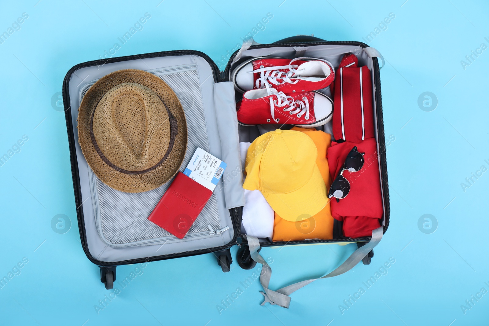 Photo of Travel abroad. Packed suitcase with passport and ticket on light blue background, top view