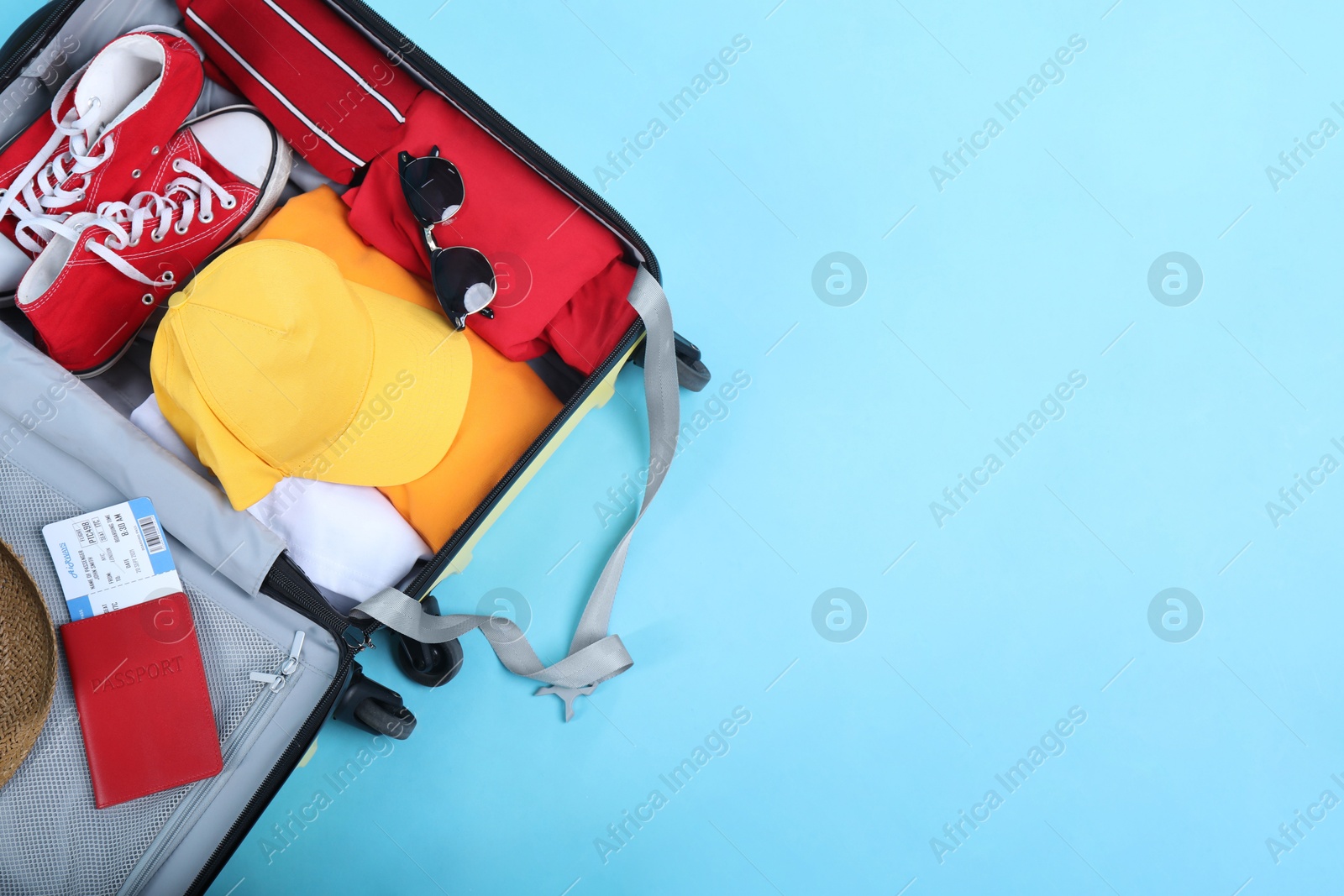 Photo of Travel abroad. Packed suitcase with passport and ticket on light blue background, top view. Space for text