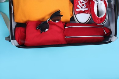 Photo of Travel abroad. Packed suitcase on light blue background, top view. Space for text